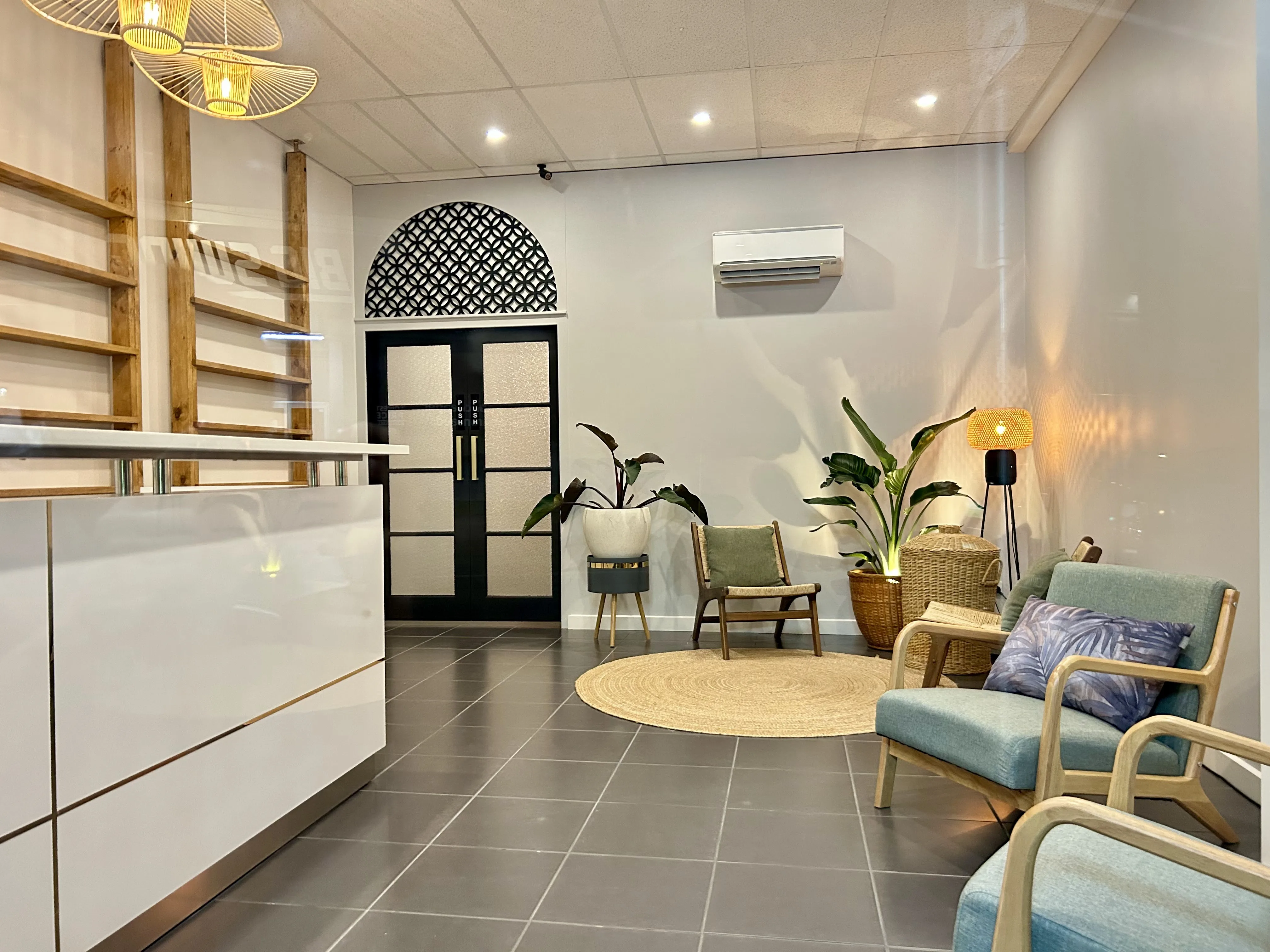 Kew waiting room — white reception desk, arched black lattice door, jute rug, teal rattan chairs